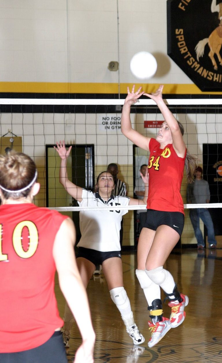 Robyn Smith Everson in a red number 34 jersey leaping to set the ball at the net