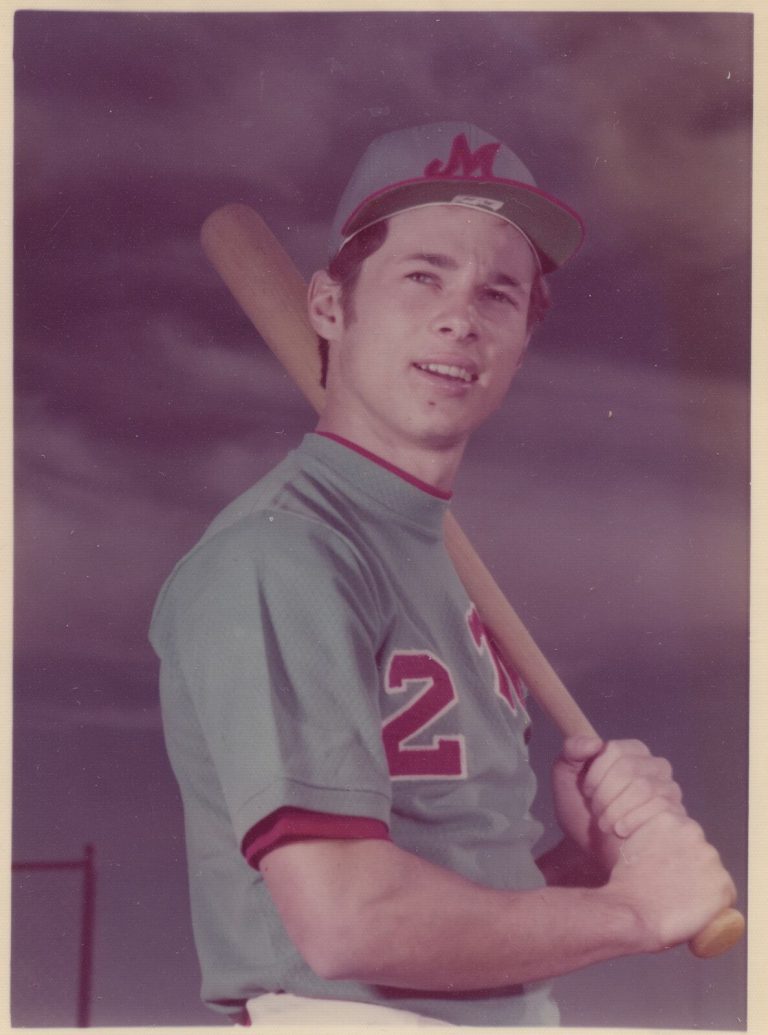 1974 Monterey State Champion Baseball Team player in a gray Monterey jersey and cap posing with a bat on one shoulder